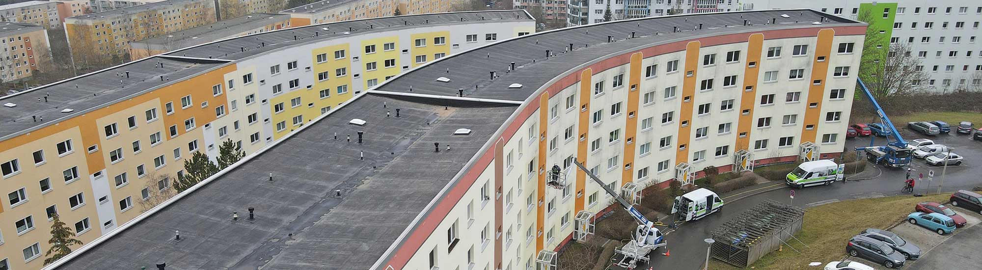 FassadenFix-Kolonne reinigt einen Wohnblock von der Hebebühne — ohne Hochdruck, mit Abwasserauffangsystem.